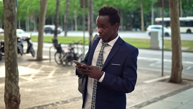 African American businessman holding mobile phone wearing blue suit and using modern smartphone near office. Business concept