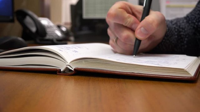 with a black pen, a young man writes in his notebook.
