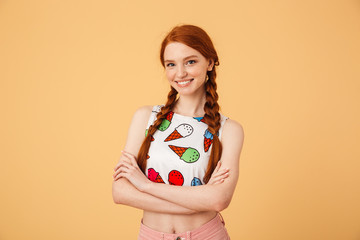 Smiling beautiful redhead woman dressed in ice cream printed t-shirt posing isolated over yellow...