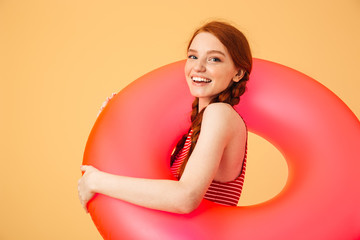 Smiling young beautiful redhead woman posing isolated over yellow background holding rubber ring.