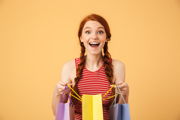 Shocked surprised young beautiful redhead woman posing isolated over yellow background holding...
