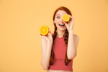 Happy  young beautiful redhead woman posing isolated over yellow background holding orange.