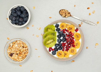 Top view of smoothie bowl with blueberries, pomegranate, kiwi, banana and granola on grey table. Healthy breakfast. Vegan food.