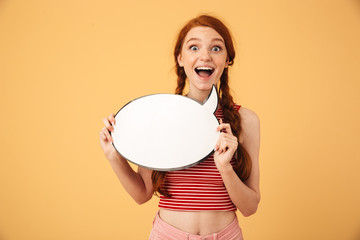Happy  young beautiful redhead woman posing isolated over yellow background holding speech bubble.