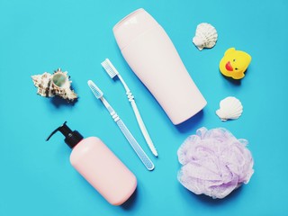 View from above liquid soap, two toothbrushes, sponge, seashells and yellow rubber duck on a blue background. Flat lay toiletries set, family cosmetics