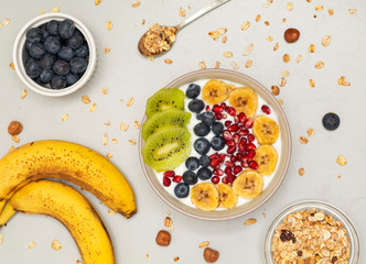 Smoothie bowl with blueberries, bananas, kiwi, pomegranates and granola. Breakfast smoothie bowl on gray background, top view. Vegan diet food concept. 