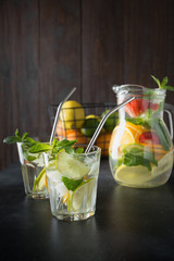 Detox lemonade with lime, orange, lemon, strawberry in glass and jar. Summer healthy freshness drink. Dark wooden background.