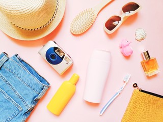 Flat lay girly photo. Clothes, cosmetics and accessories for summer travel. Flat lay stuff. Blue jeans, sun hat, camera, yellow sunscreen bottle, shampoo, wooden comb, sunglasses, perfume, toothbrush