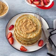 Vegan pancakes with flax seeds, peanut butter, strawberry and vegan milk on a white plate on a gray background. delicious homemade healthy food	