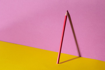 red pencil with a shadow on a trendy purple and yellow background.space for text