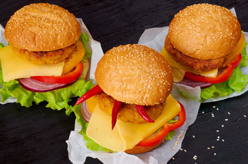 Three veggie burgers with falafel, salad, cheese, tomatoes and chili peppers on the black background. Traditional American fast food. Side view