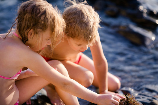 Blonde girl and bpy playind near sea water during summer holidays. Attractive child having fun on a tropical beach, playing with stones and water