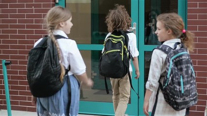 Children With Backpacks Going To School. Two Boys And Two Girls Are Returning On Lessons Near The School. Back To School