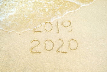 Fototapeta na wymiar Happy new year. 2020 and 2019 written on the sand where 2019 is getting washed away by the wave