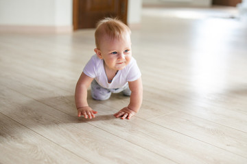 Cute little baby boy lying on hardwood and smiling. Child crawling over wooden parquet and looking up with happy face. View from above. Copyspace