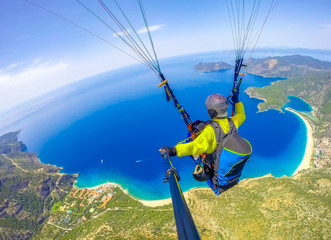 Paragliding in the sky. Paraglider tandem flying over the sea with blue water and mountains in...