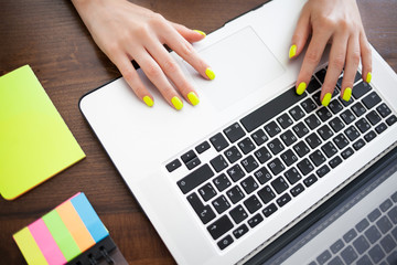 Women's hands with trend yellow manicure typing text on a laptop keyboard.
