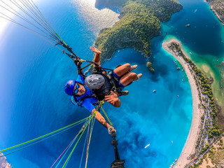 Paragliding in the sky. Paraglider tandem flying over the sea with blue water and mountains in...