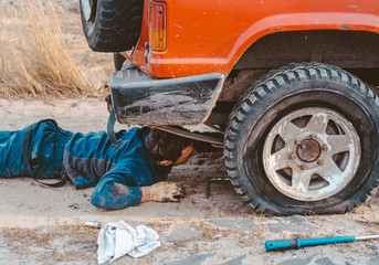man lies under a 4x4 car on a dirt road © teksomolika