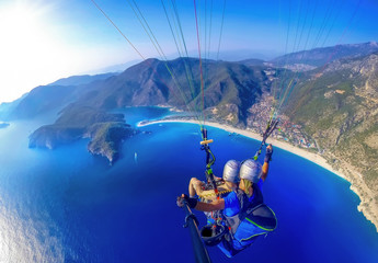 Paragliding in the sky. Paraglider tandem flying over the sea with blue water and mountains in...
