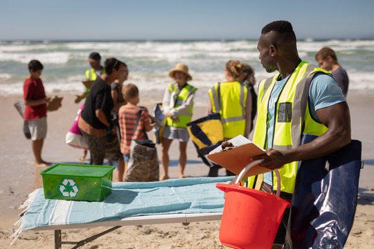Volunteer standing with bucket and clipboard on the beach