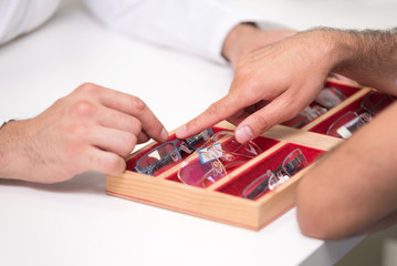 ophthalmologist hands close up, showing a tray with different glasses to a customer .