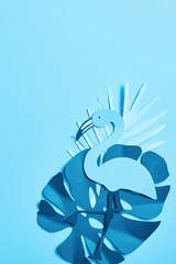 top view of blue minimalistic paper cut palm leaves and flamingo on blue background with copy space
