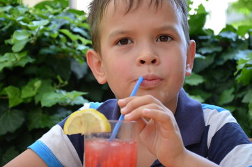 The boy is holding Healthy watermelon smoothie jar with mint and striped straws on a wood background.