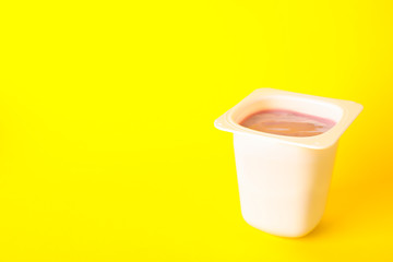 Plastic cup with yogurt on color background, space for text