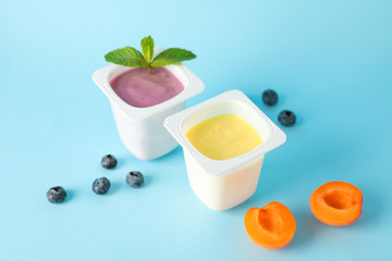 Plastic cups with yogurt and fruits on color background, space for text