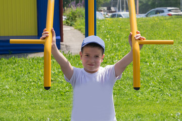 Fototapeta premium The boy is engaged in the yard on the street simulator. The child smiles while doing sports.