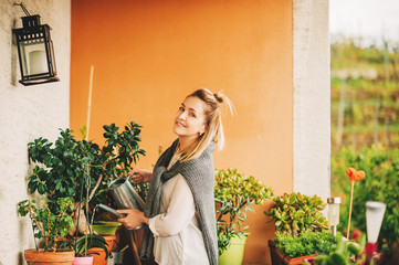 Portrait of beautiful woman watering green plants on the balcony, small cozy garden in apartment