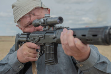 elderly man, war veteran, chooses sniper rifle with telescopic sight in gun shop. Pensioner wants to protect your home. concept of weapons for self-defense
