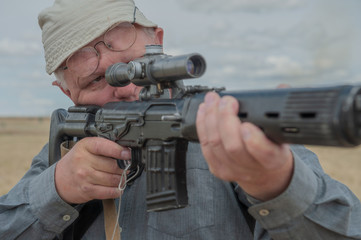 Fototapeta premium elderly man, war veteran, chooses sniper rifle with telescopic sight in gun shop. Pensioner wants to protect your home. concept of weapons for self-defense