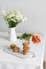 Fresh homemade delicious carrot muffins with dried fruits and nuts on the white plate, chamomile bouquet and carrot on the table. Copy space