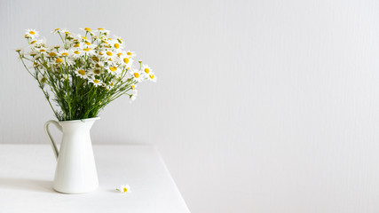 Daisy chamomile bouquet in vase on white table. Side view with copy space. Country style, interior