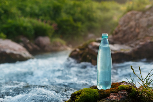 Plastic bottle with fresh drinking water on the background of a mountain stream, in the wild. ool fresh water