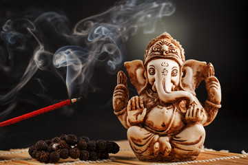 Hindu god Ganesh on a black background. Rudraksha statue and rosary on a wooden table with a red...