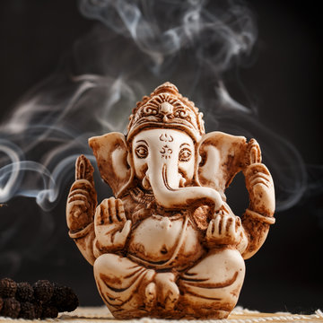 Hindu god Ganesh on a black background. Statue with incense smoke aromo sticks