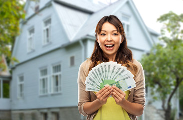 mortgage, real estate and property concept - happy asian young woman holding hundreds of euro money...
