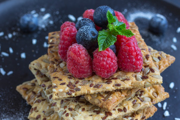 Cookies with whole grains. Raspberry and blueberry berries with icing sugar on top. black background.