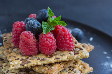 Cookies with whole grains. Raspberry and blueberry berries with icing sugar on top. black background.