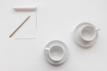 Top view of two empty coffee cups with paper note and wooden pencil put on clean white table plate in the living room and soft sunlight from window. Selective focus and copy space.