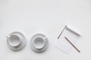Top view of two empty coffee cups with paper note and wooden pencil put on clean white table plate in the living room and soft sunlight from window. Selective focus and copy space.
