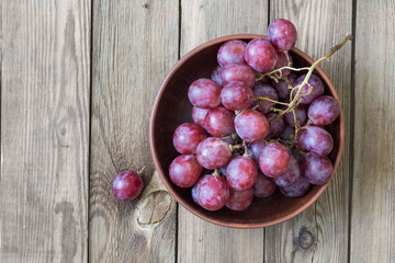 Bunch of red grapes in a bowl on a wooden table. Copy space. Rustic style