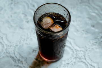 Brown drink with ice in a glass. Refreshing dark drink with ice cubes