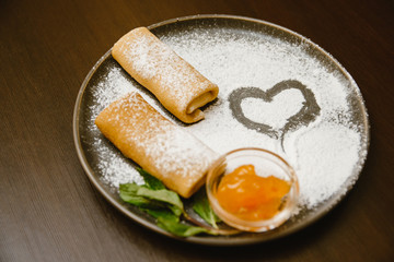pancakes rolls on a dark plate with powdered sugar, jam and mint. Delicious dessert