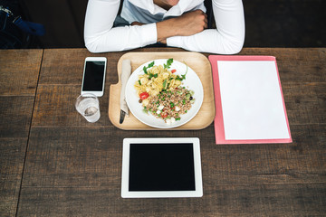 Young businessman dressed casual sitting at a restaurant table with a plate of pasta and spelled, a tablet, a smart phone and a work file - Millennial at lunch break - Top view