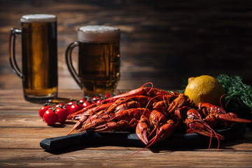 red lobsters, tomatoes, dill, lemon and glasses with beer on wooden surface