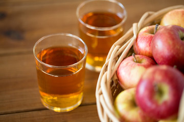 fruits, food and harvest concept - apples in wicker basket and glasses of juice on wooden table
